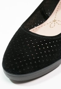 Zapato negro de lona perforado tipo slip-on con textura suave de ante y punta redondeada. Presenta una suela de goma gris y un forro interior suave.