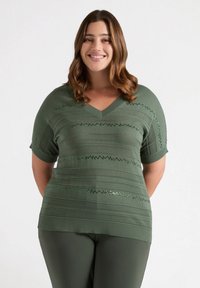 Groene gebreide top met een V-hals en korte mouwen, voorzien van horizontale textuurstrepen en versieringen. Gladde stof met geribbelde details.