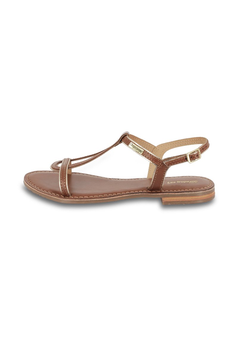 Sandalia de cuero marrón con suela plana, que presenta un diseño de tiras delgadas y cierre con hebilla. Incluye costuras detalladas y forma de puntera redonda.