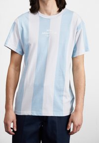 Světle modré a bílé pruhované bavlněné tričko s kulatým výstřihem a logem "Nike Athletic Club" uprostřed. Krátké rukávy.