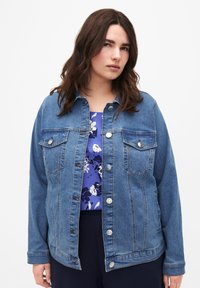 Keskmise sinise värvusega teksajakk klassikalise disainiga; kaks rinna taskut, hõbedased nööbid ja lõdvestatud lõige, kantud lillelise särk.}}