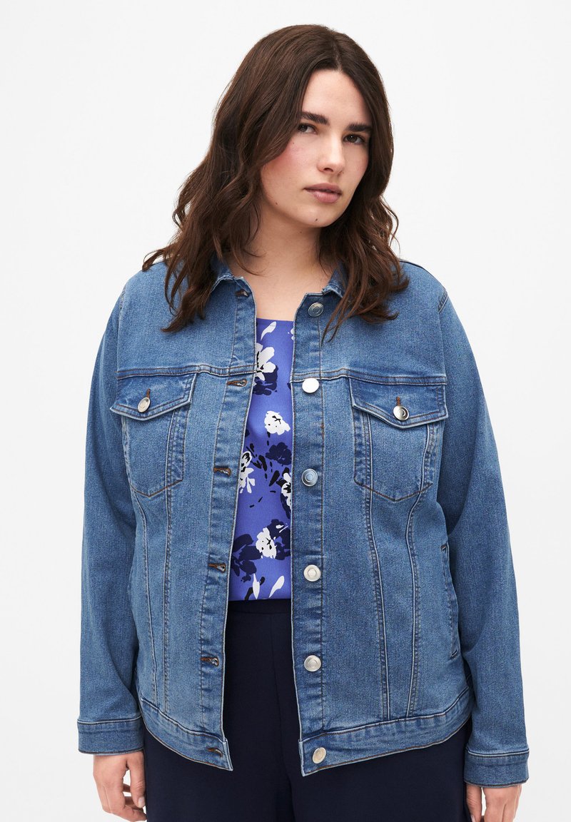 Keskmise sinise värvusega teksajakk klassikalise disainiga; kaks rinna taskut, hõbedased nööbid ja lõdvestatud lõige, kantud lillelise särk.}}