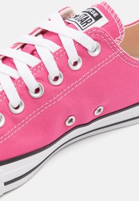 Różowe płócienne sneakersy z białymi sznurowadłami, metalowymi oczkami i gumową podeszwą w czarno-białe paski; posiadają metkę z logo na języku.