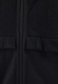 Chaqueta negra con cremallera, con una parte superior de tela texturizada y una sección inferior lisa. Presenta una cremallera oculta y un detalle de costura en contraste.