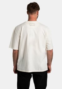 Camiseta blanca de manga corta con un corte relajado. Presenta un logo visible en la parte posterior, tejido suave y un dobladillo recto.
