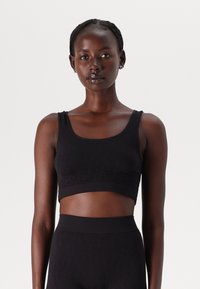 Black sports bra with a smooth, stretchy texture, featuring a scoop neckline and wide straps, paired with matching high-waisted leggings.