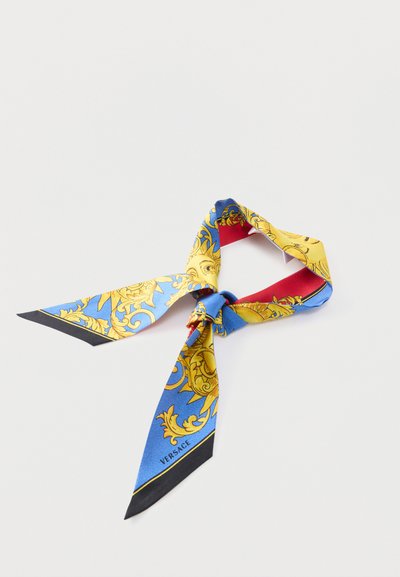 Μεταξωτό φουλάρι με μπλε, κίτρινα και κόκκινα μπαρόκ σχέδια, δεμένο χαλαρά σε κόμπο, με την ετικέτα "Versace" στο μπλε τμήμα.
