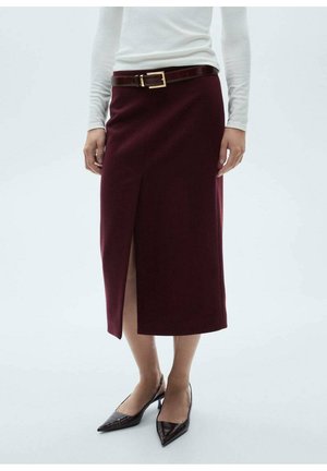 Kobieta w bordo midi spódnicy z przednim rozcięciem, brązowym pasku, białej bluzce z długim rękawem i czarnych szpilkach z noskiem w szpic.