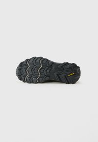 Fekete, strapabíró cipőtalp mély barázdákkal és sárga Goodyear logóval a sarkán, sima fehér háttér előtt fényképezve.