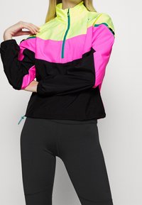 Colorful windbreaker featuring a bright yellow and pink upper with a black lower section, half-zip closure, and elastic cuffs.
