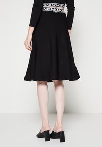Gonna nera fino al ginocchio realizzata in tessuto elasticizzato, con design svasato e una cintura decorata con il motivo delle lettere "MK."