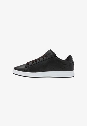 Zapatillas de piel negra con un acabado suave, suela de goma blanca, cordones marrón oscuro y pequeñas perforaciones en los laterales para ventilación.