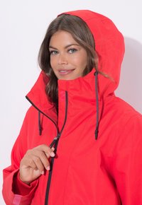 Czerwona wodoodporna kurtka z wysokim kołnierzem i regulowanym kapturem. Posiada przedni zamek błyskawiczny oraz elastyczne mankiety z kontrastowymi czarnymi akcentami.
