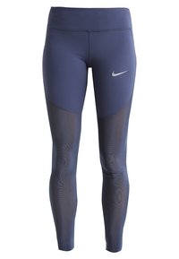 Marina träningsleggings med bred midja, slät textur och nätpaneler på sidorna. Har en silvrig Nike-logga.