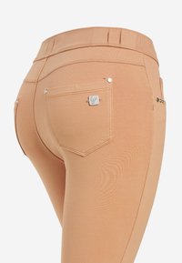 Un jean couleur pêche au design ajusté, avec une taille haute, des coutures décoratives et des éléments en métal argenté sur les poches arrière.