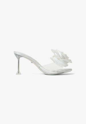 Weiße Mules mit Absatz, ausgestattet mit einem transparenten Riemen und einem großen Satinblütenakzent. Der Absatz ist klar und hat eine geometrische Basis.