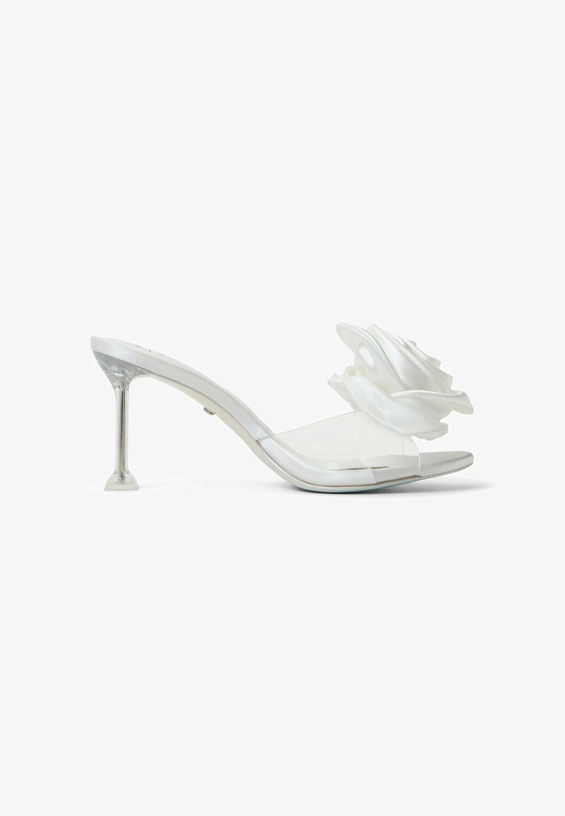 Mules blancs à talons avec une bride transparente et un grand accent floral en satin. Le talon est transparent avec une base géométrique.