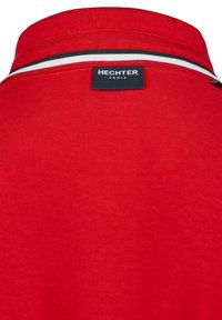 T-shirt polo rouge avec un col côtelé, des accents rayés blancs et noirs, et une étiquette brodée avec "HECHTER PARIS" au dos.