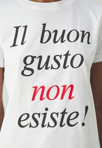 Biała bawełniana koszulka z wyraźnym czarno-czerwonym napisem: "Il buon gusto non esiste!" w różnych stylach i rozmiarach czcionek.