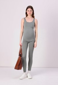 Conjunto de maternidade com uma camisola cinza justa e leggings, complementado por ténis brancos e uma mala de couro castanho. Tecido suave e elástico.