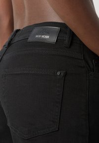 Black denim jeans featuring a leather MOS MOSH tag, visible stitching, and two rear pockets with a button detail.