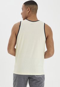 Lys beige tanktop med marineblå trim, lavet af blødt stof. Simpelt design uden mønstre, med en afslappet pasform og en rund halsudskæring.