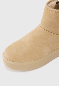 Bottines en suède beige avec un bout arrondi, texture lisse et une semelle en caoutchouc épaisse. Présente des coutures minimales et un design simple.