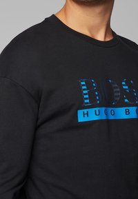 Felpa nera in cotone con logo testuale a strisce blu "BOSS HUGO BOSS" centrato sul petto. Collo rotondo, vestibilità comoda.