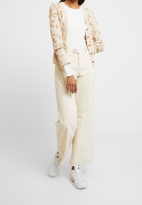 Cardigan beige con patrón animal, suéter crema, pantalones anchos de tiro alto crema y zapatillas blancas con acentos grises.