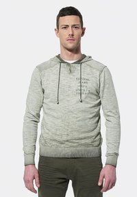 Lichtgroene hoodie met een textuurafwerking, trekkoorden en een grafisch ontwerp aan de voorkant. Geribde manchetten en zoom, gedragen over olijfgroene broek.