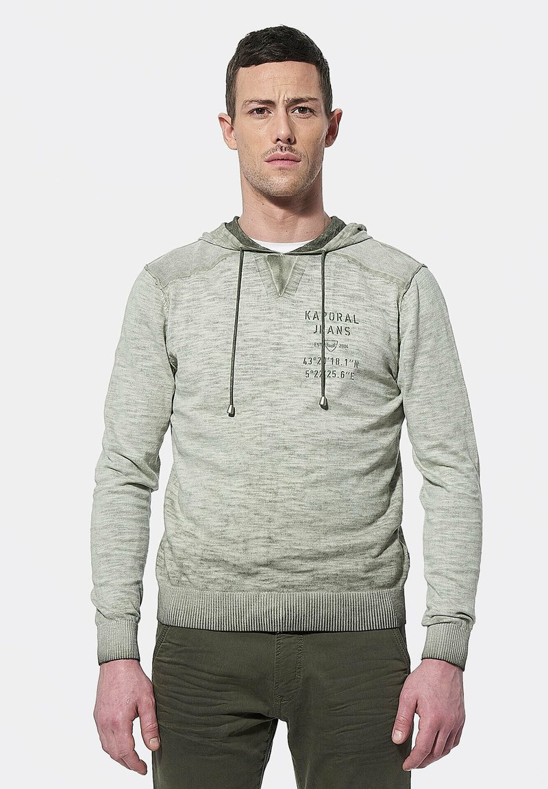 Lichtgroene hoodie met een textuurafwerking, trekkoorden en een grafisch ontwerp aan de voorkant. Geribde manchetten en zoom, gedragen over olijfgroene broek.