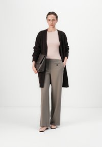 Dunkelbrauner Cardigan, hellrosa Oberteil, graue Hose und beigefarbene Ballerinas. Das Outfit zeichnet sich durch ein elegantes Design und eine strukturierte Handtasche mit Akzentdetails aus.