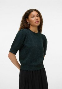 Pull en maille court à manches courtes de couleur vert foncé avec un col rond, un tissu texturé et des manches légèrement bouffantes, associé à une jupe noire.
