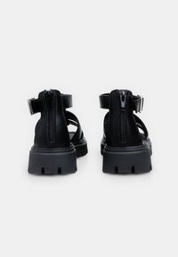 Czarne sandały z zapięciem na zamek z tyłu, regulowanym paskiem, trwałą podeszwą oraz wieloma wycięciami dla lepszej wentylacji.