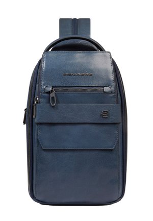 Kompakter dunkelblauer Lederrucksack mit Tragegurt, vorderer Reißverschlusstasche, Klappentasche und Metalllogo auf weißem Hintergrund.