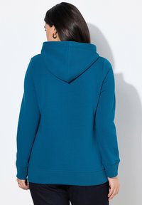 Felpa con cappuccio color teal, con maniche lunghe, polsini e orlo a costine. Tessuto morbido, presenta una vestibilità comoda e dettagli di cucitura minimal.