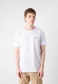 Tricou alb din bumbac, cu guler rotund și mâneci scurte. Prezintă un mic logo negru centrala pe piept. Textură moale, croială lejeră.