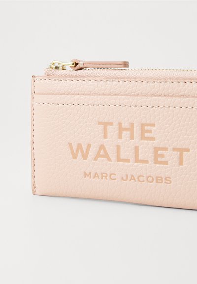 Maigi rozā ādas maciņš ar teksturētu virsmu, rotāts ar zelta aksesuāriem un iegravētiem zīmoliem "THE WALLET" un "MARC JACOBS."