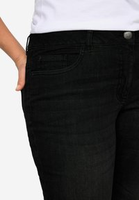 Juodi džinsai iš denim medžiagos su nedideliu elastingumu, penkių kišenių dizainu, mygtuko uždarymu ir subtilia toniniu siuvinėjimu. Sklandus paviršius.