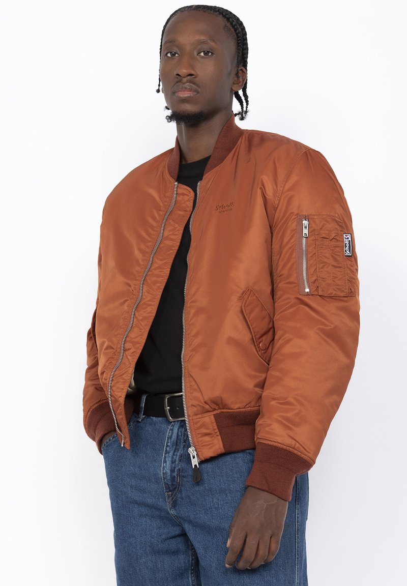 Bruine bomberjack met een rits aan de voorkant, gebreide manchetten en zijzakken. Beschikt over een ritszak op de mouw en logo detail op de borst.