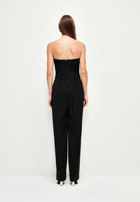 Černý pruhovaný overálek bez ramínek, s zúženými nohavicemi a přiléhavým pasem. Obsahuje zip na zadní straně a má elegantní vzhled.