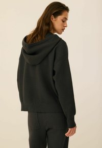 Czarny krótki hoodie wykonany z miękkiego materiału, z kapturem na sznurki i ściągaczami przy mankietach. W zestawie z pasującymi ciemnymi spodniami.