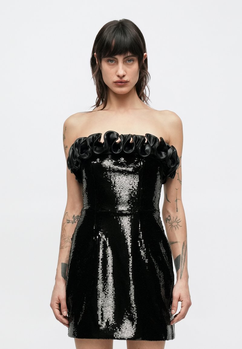 Melnas spīdīgas mini kleita ar piegulošu siluetu, bezplecu dizains un melni rušķainas detaļas pie kakla izgriezuma.