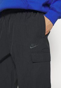 Svarta Nike cargo-byxor med en texturerad yta, med en zipficka, elastisk midja och en präglad logotyp på låret.