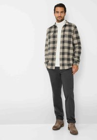 Camicia di flanella a quadri neri e beige, indossata sopra un dolcevita bianco. Pantaloni scuri e stivali casual marroni completano l'outfit.