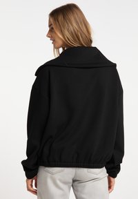 Felpa nera oversize con colletto ampio, orlo elastico e vestibilità rilassata. Il materiale sembra morbido con una texture liscia.