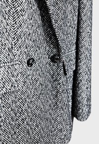 Sort og hvidt hundetand mønster blazer med tekstureret stof, der har to sorte knapper og strukturerede revers. Skræddersyet pasform.