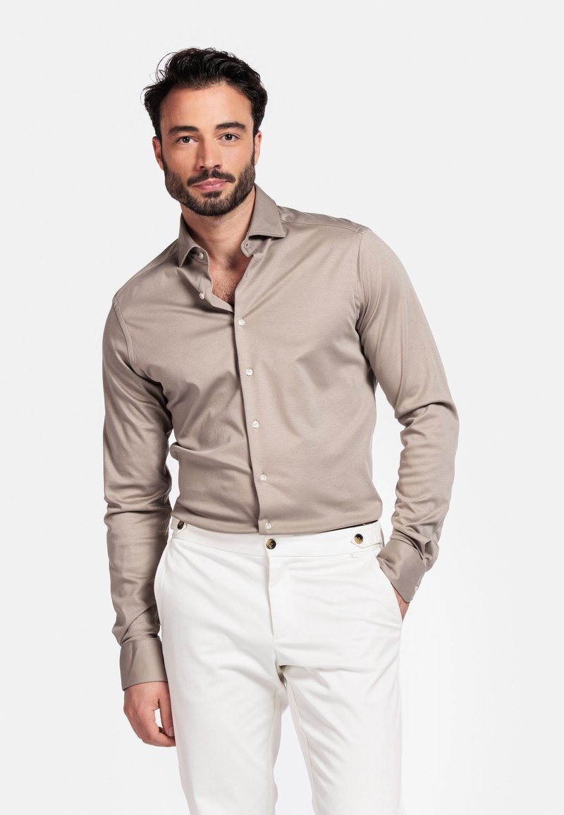 Lichtbruin overhemd met lange mouwen, een button-down kraag en een soepele textuur, gecombineerd met witte broek met gouden accenten.