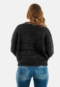 Suéter negro de pelaje suave con un escote redondeado y detalles decorativos de cuentas en la parte posterior, combinado con jeans ajustados azules que presentan costuras de bolsillo distintivas.
