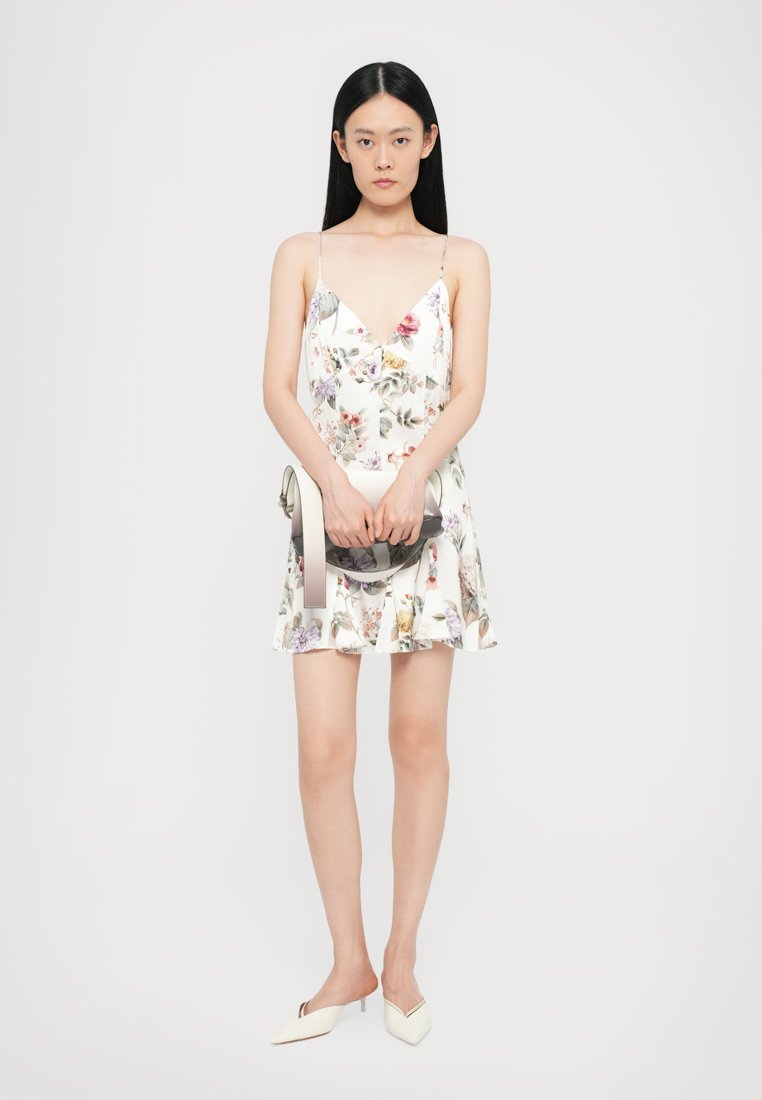 Robe sans manches à imprimé floral avec décolleté en V et ourlet évasé. Elle présente un tissu lisse et léger en blanc avec des motifs de fleurs multicolores.